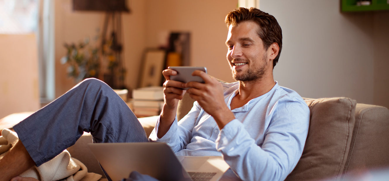 A man is on his couch using his mobile phone.